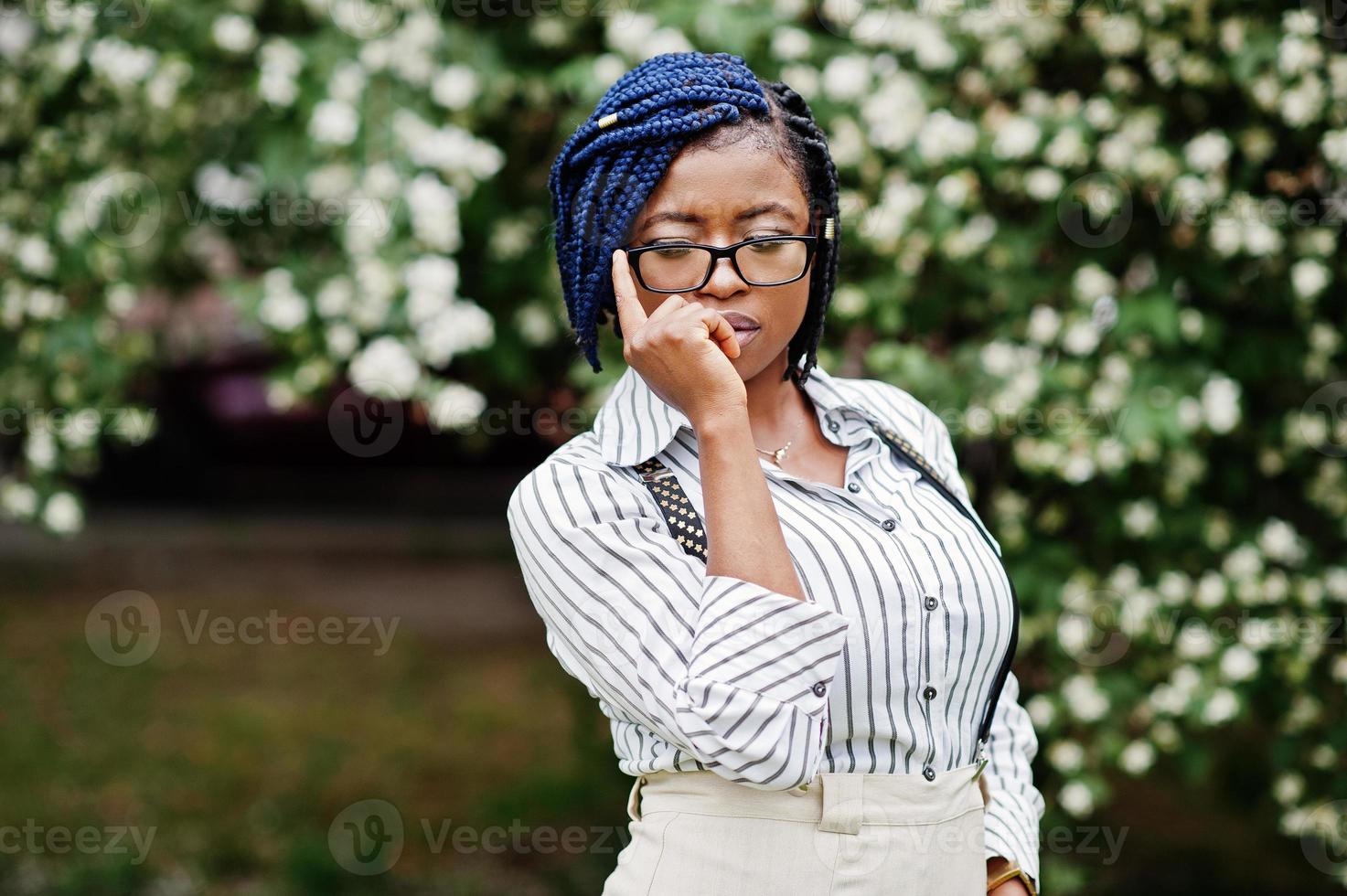 stijlvolle Afro-Amerikaanse zakenvrouw op broek met jarretel en blouse, bril poseerde buiten. foto