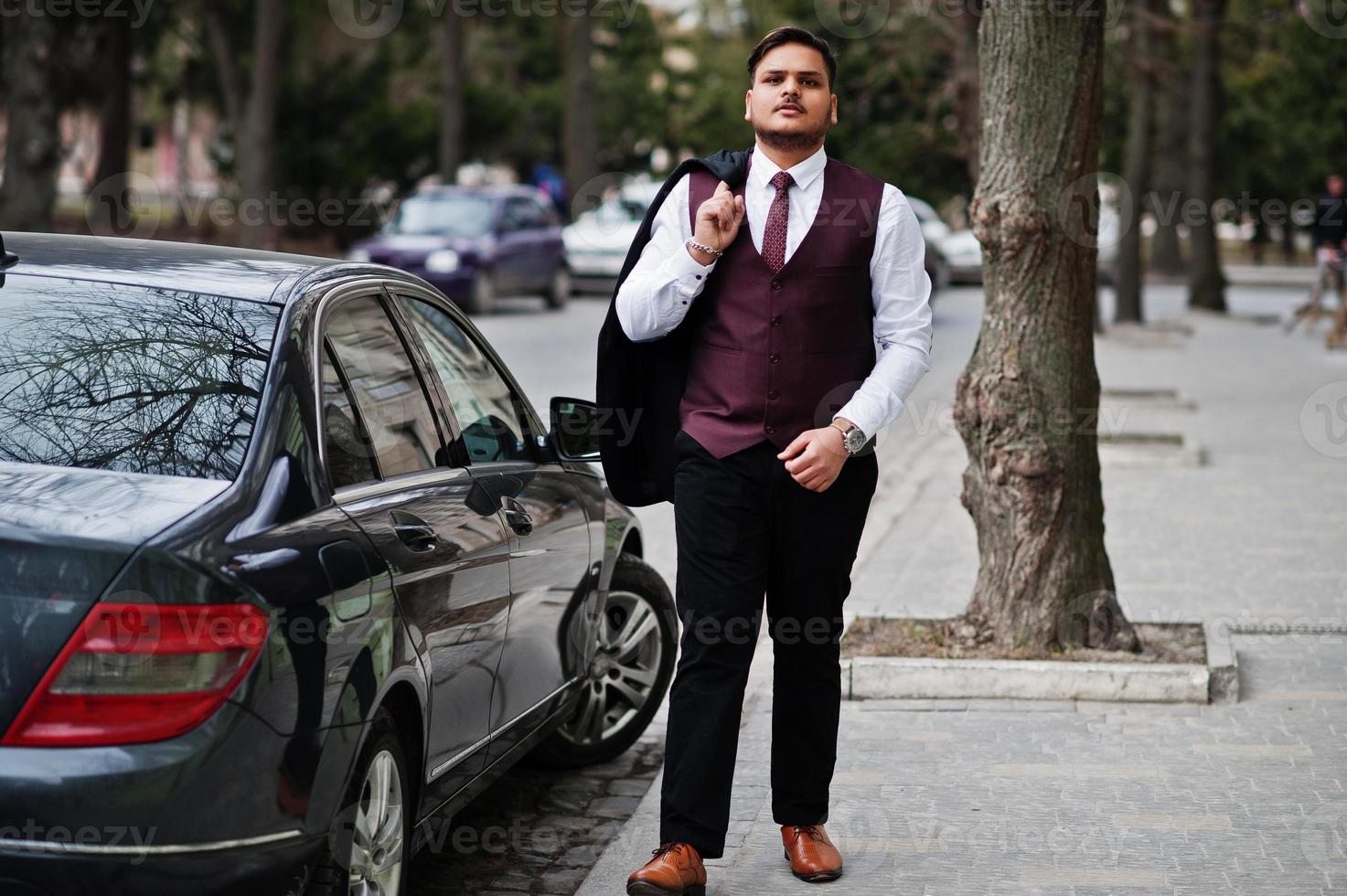 stijlvolle Indiase zakenman in formele slijtage staande tegen zwarte zakenauto op straat van de stad. foto