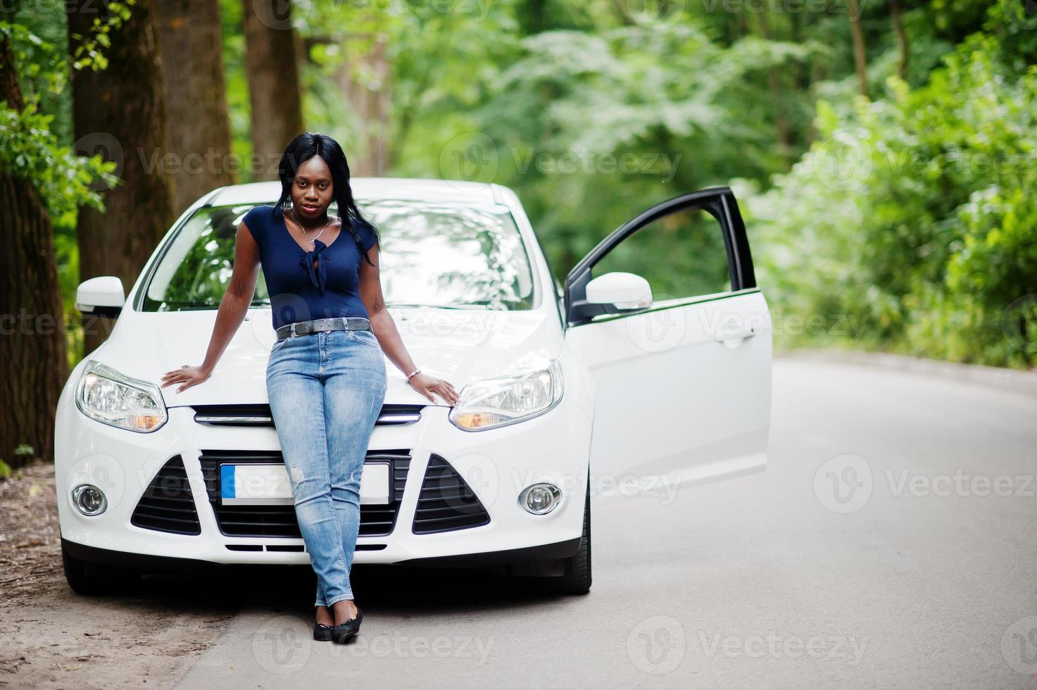 Afro-Amerikaanse vrouw poseerde tegen witte auto in bosweg. foto