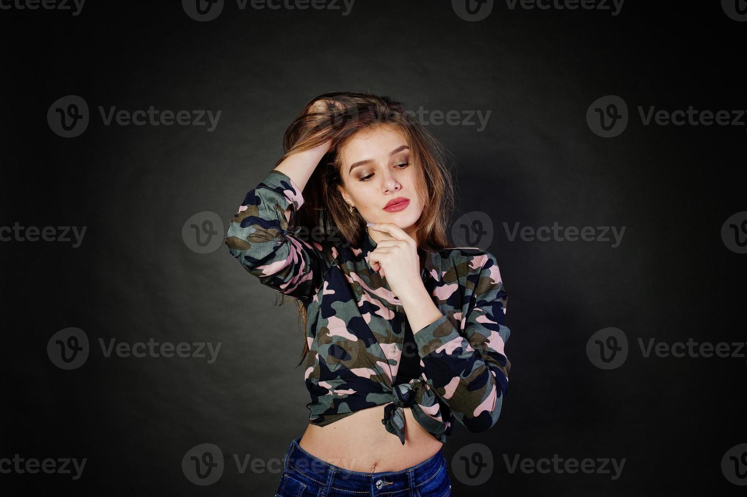 knappe brunette meisje draagt militair shirt en spijkerbroek, poseren in studio tegen een grijze achtergrond. studiomodel portret. foto