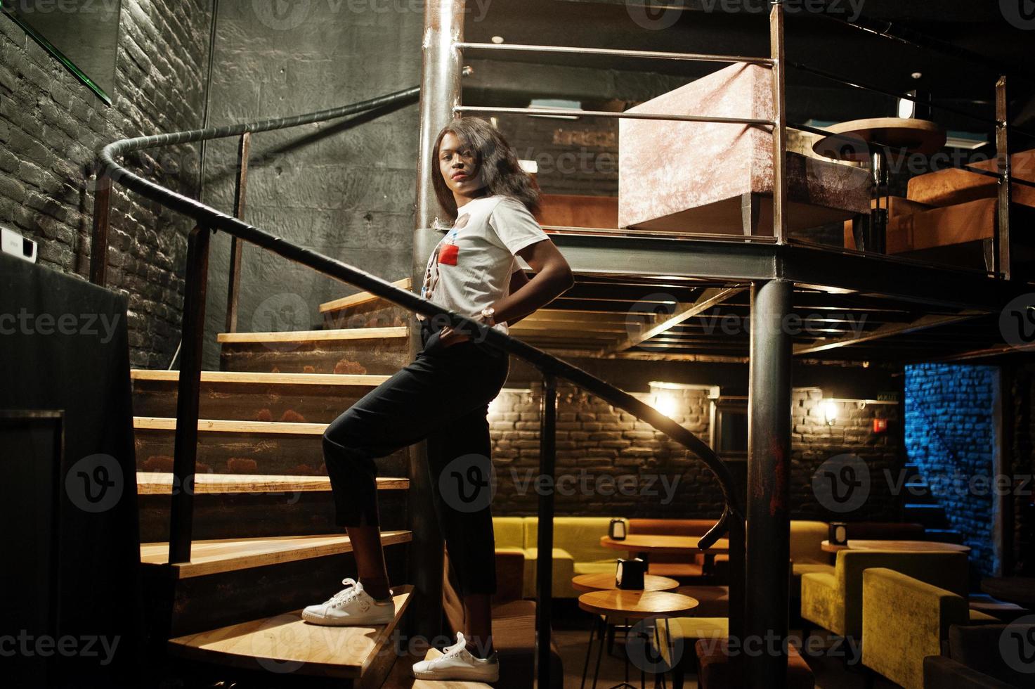 stijlvolle Afro-Amerikaanse vrouw in bedrukt t-shirt poseerde binnen stalen trappen. foto