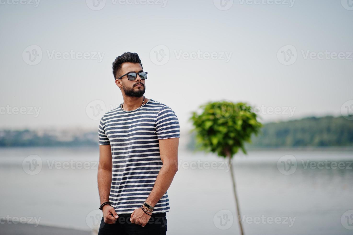 knappe lange Arabische baard man model op gestript shirt buiten geposeerd. modieuze Arabische man bij zonnebril. foto