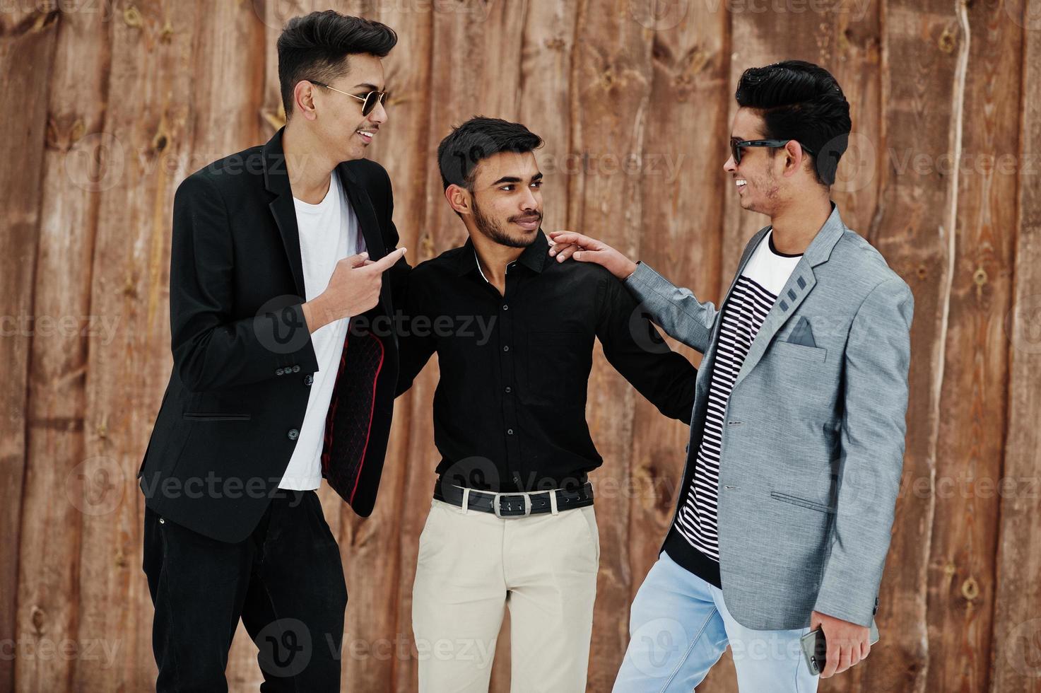 groep van drie casual jonge indiaan mans poseerde tegen houten achtergrond. foto
