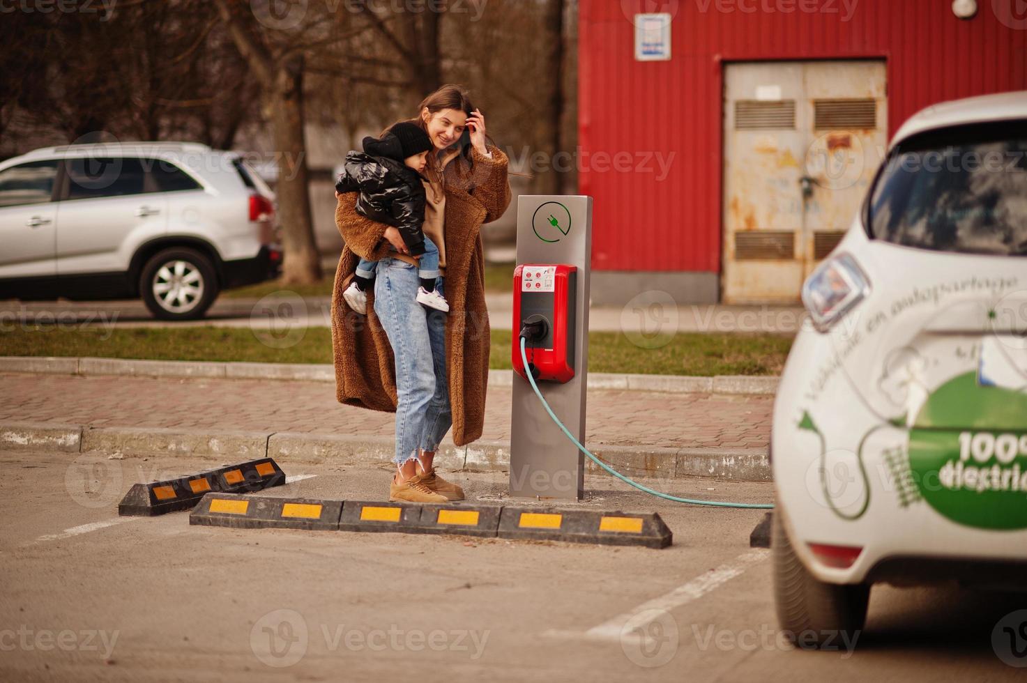 jonge moeder met kind elektrische auto opladen bij het elektrische tankstation. foto