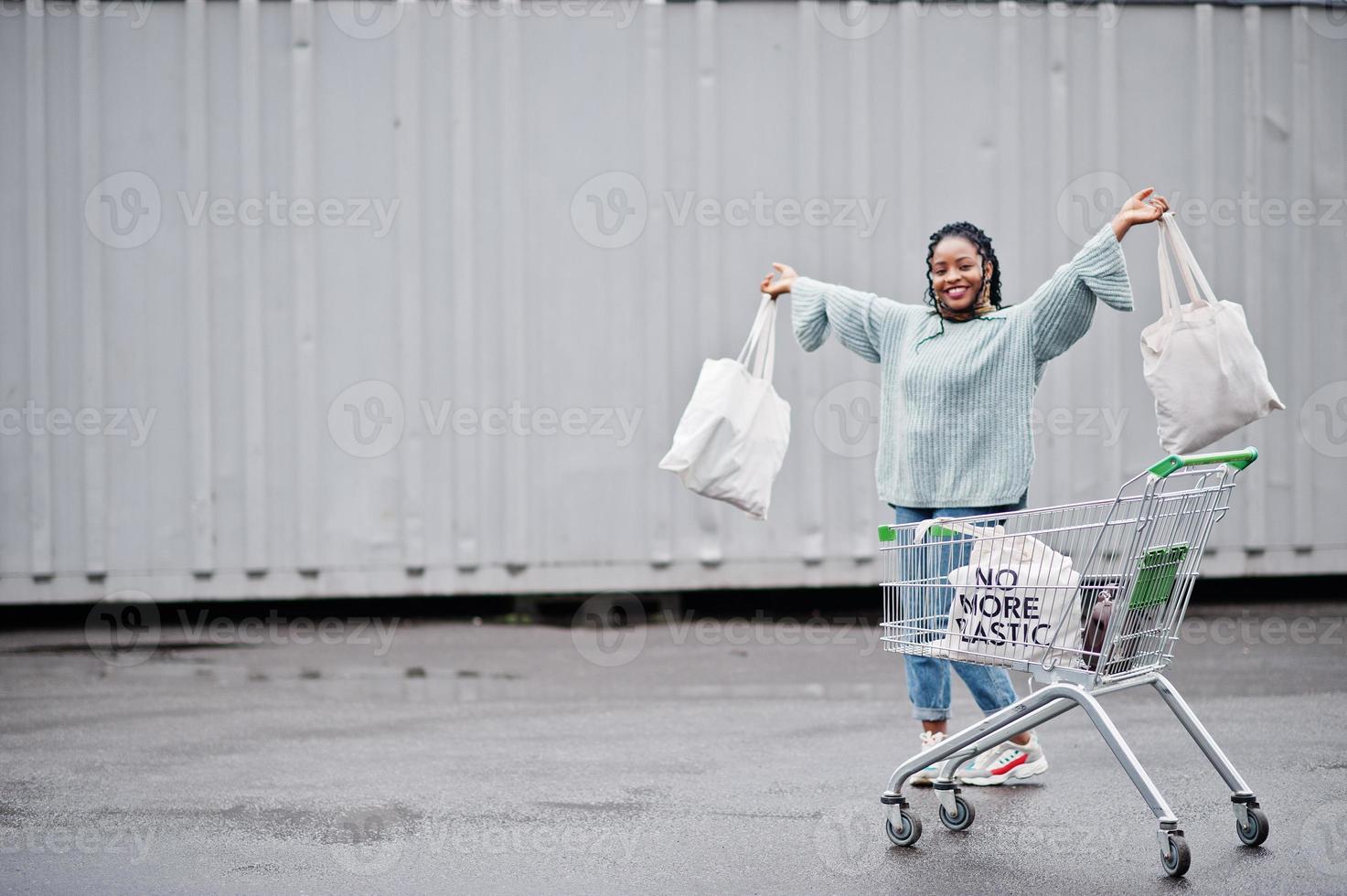 geen kunststof meer. Afrikaanse vrouw met winkelwagentje en eco-tassen poseerde buitenmarkt. foto