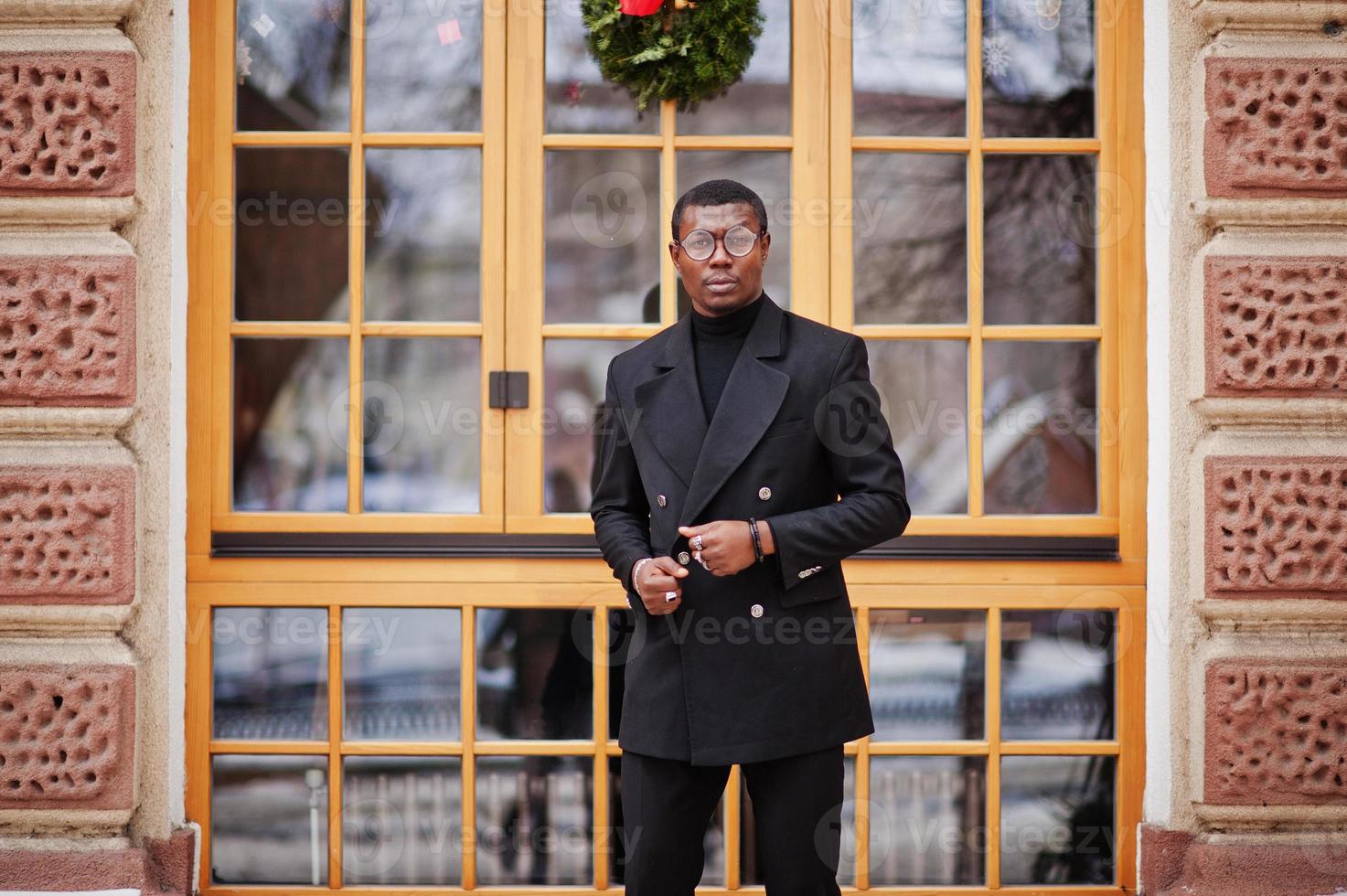 stijlvolle Afro-Amerikaanse heer in elegante zwarte jas. rijke modieuze afro man tegen raam. foto