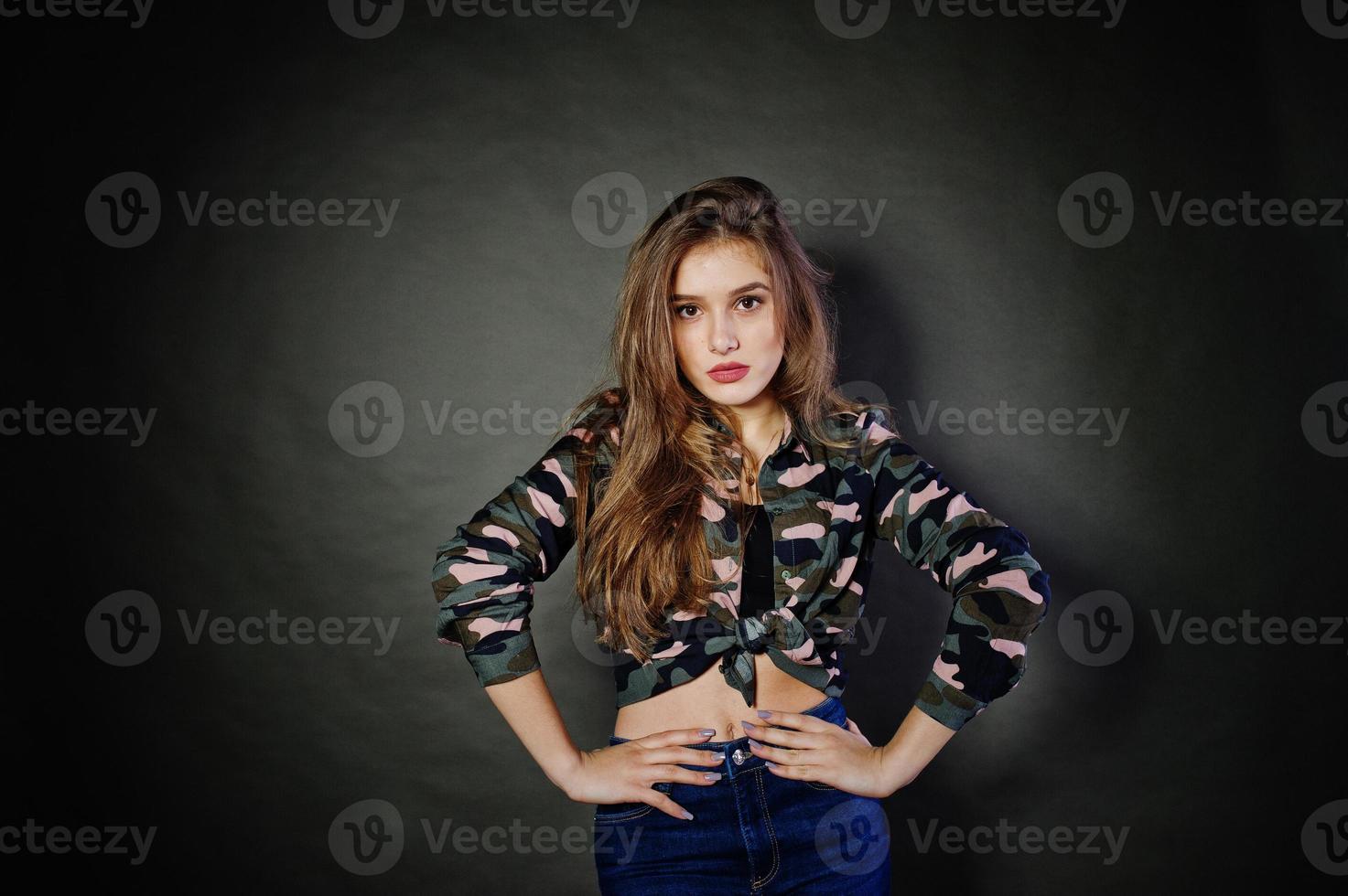 knappe brunette meisje draagt militair shirt en spijkerbroek, poseren in studio tegen een grijze achtergrond. studiomodel portret. foto