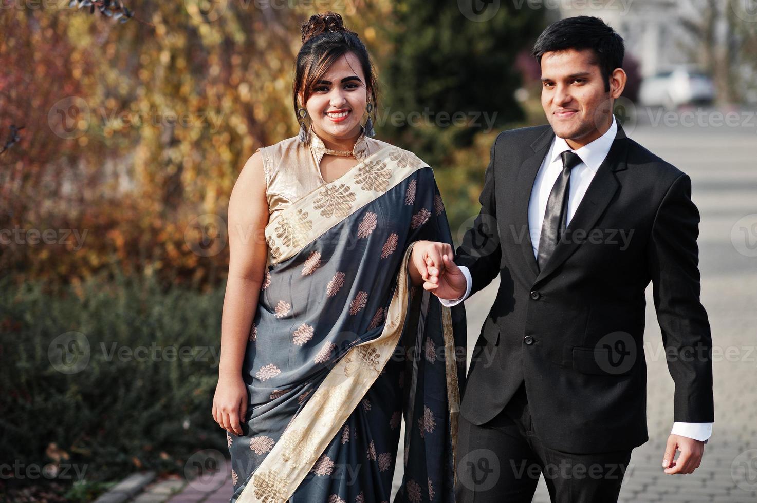 elegante en modieuze Indiase vrienden paar vrouw in saree en man in pak buiten wandelen en hand in hand. foto