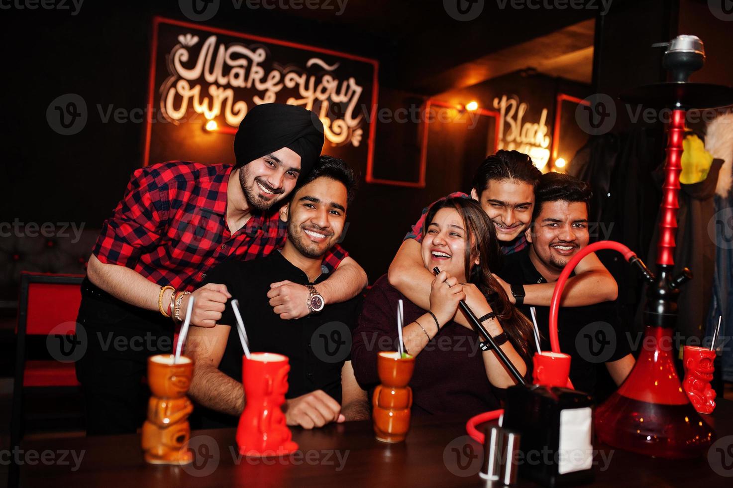 groep indische vrienden die plezier hebben en rusten in de nachtclub, cocktails drinken en waterpijp roken. foto