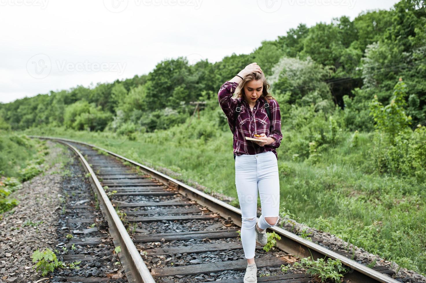 portret van een mooi blond meisje in tartan shirt wandelen op de spoorlijn met kaart in haar handen. foto