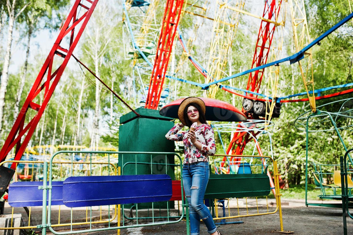 portret van brunette meisje in roze bril en hoed met ijs in pretpark. foto