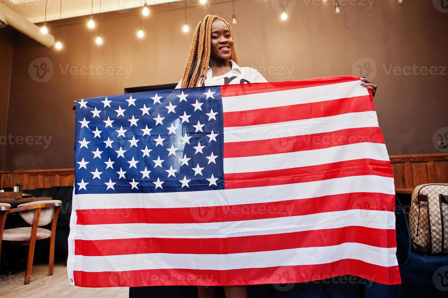 mooie Afrikaanse vrouw in stijlvolle casual kleding poseren met usa vlag in handen in kantoor. foto