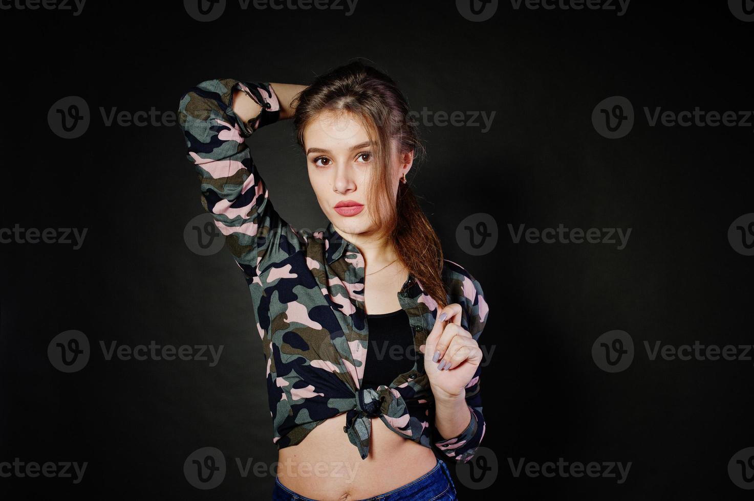 knappe brunette meisje draagt militair shirt en spijkerbroek, poseren in studio tegen een grijze achtergrond. studiomodel portret. foto