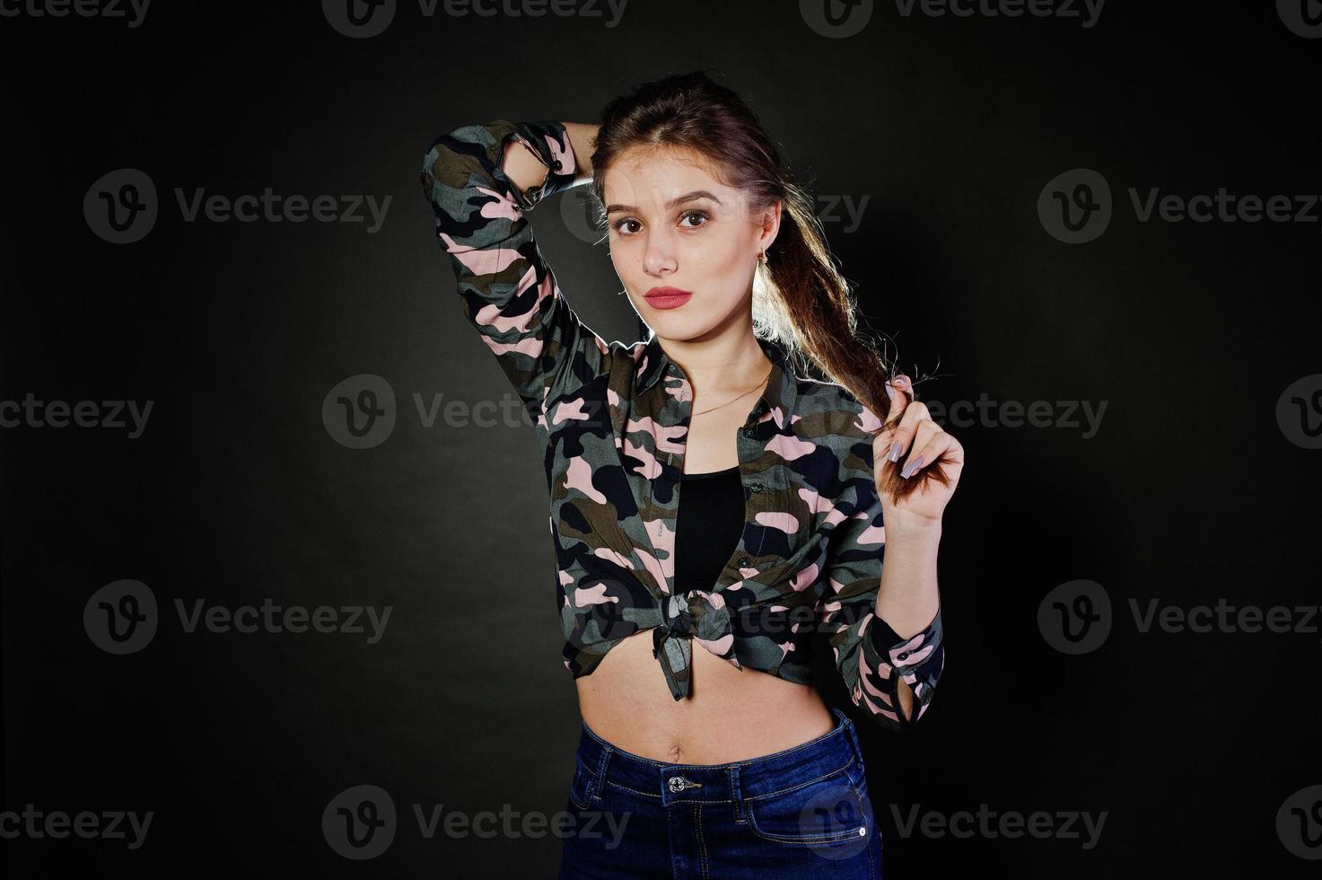 knappe brunette meisje draagt militair shirt en spijkerbroek, poseren in studio tegen een grijze achtergrond. studiomodel portret. foto