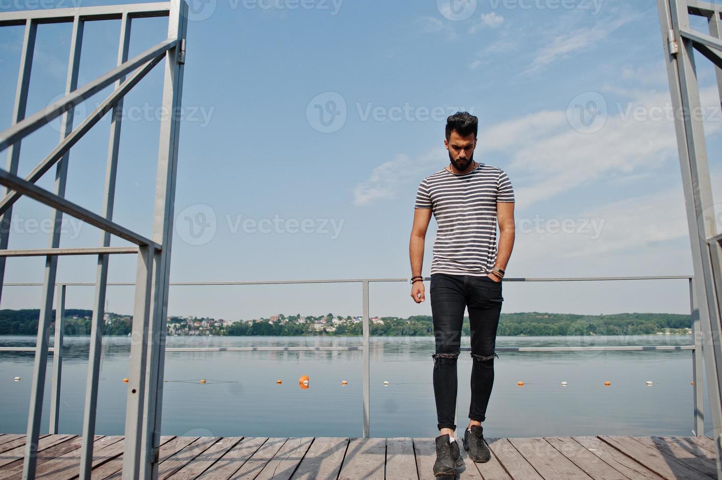 knappe lange arabische baard man model op gestript shirt poseerde buiten op de pier van het meer. modieuze Arabische man. foto