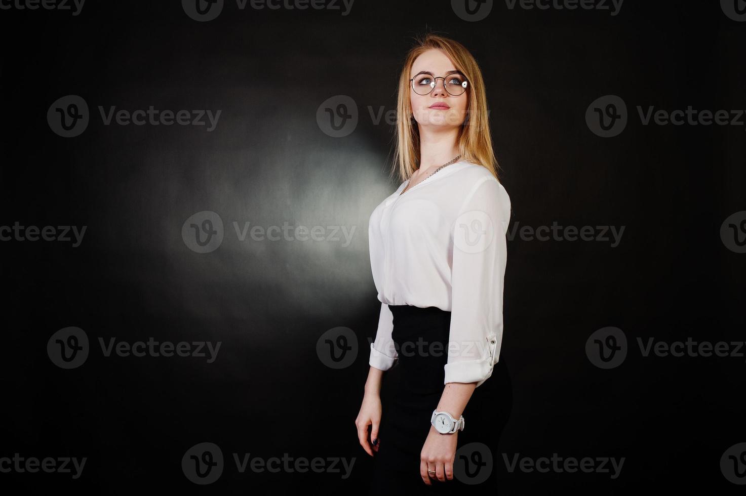 studio portret van blonde zakenvrouw in glazen, witte blouse en zwarte rok tegen een donkere achtergrond. succesvolle vrouw en stijlvol meisje concept. foto