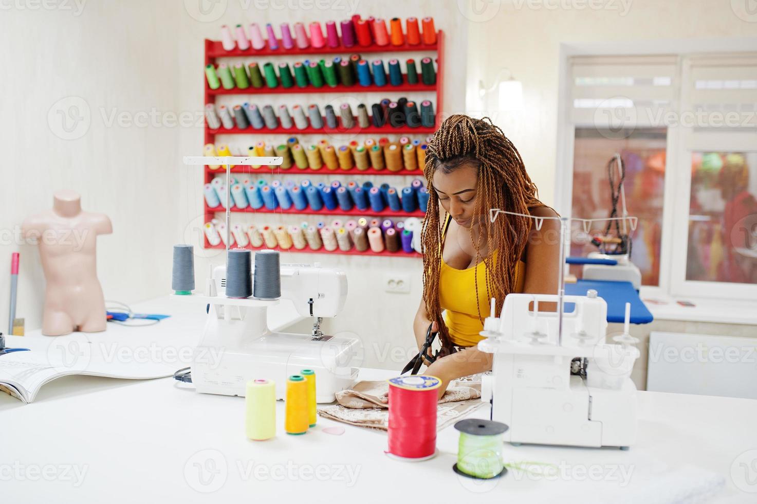 jonge afrikaanse naaister vrouw naait kleding op de naaimachine en gebruikt een schaar op het kleermakerskantoor. zwarte naaister vrouwen. foto