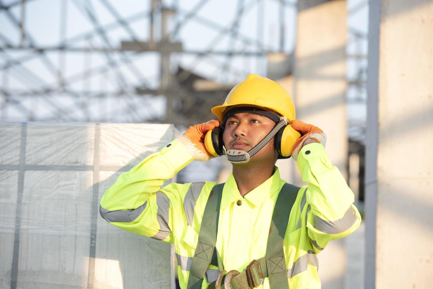 Aziatische ingenieurs in veiligheidshelmen en veiligheidsvesten voor werknemers met beschermende koptelefoons op bouwplaatsen. foto