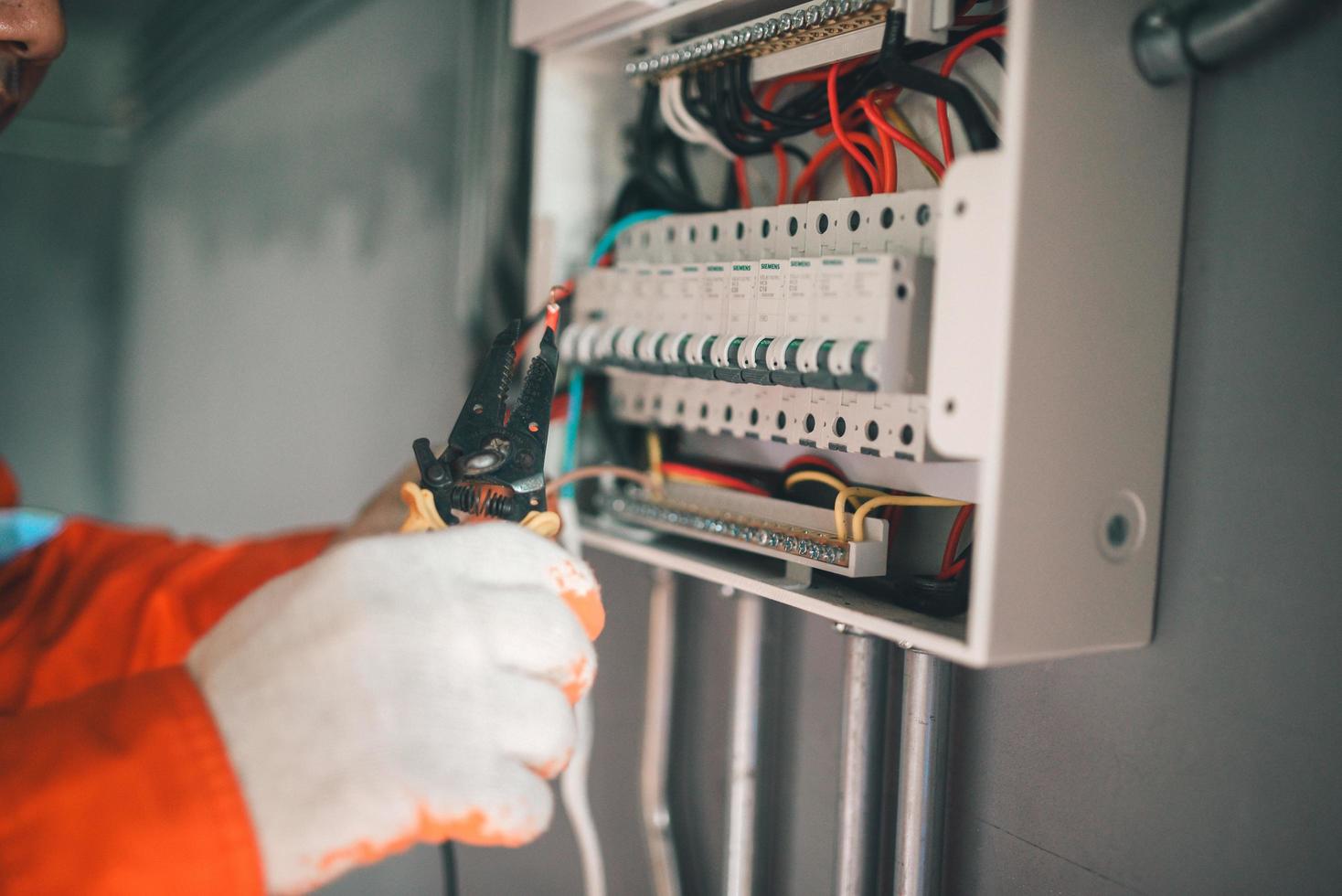 zijaanzicht van een knappe Aziatische elektricien die een elektriciteitskast repareert met een tang in de gang. foto