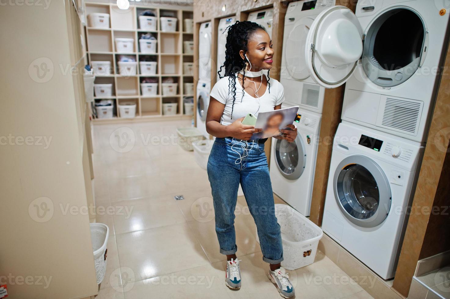 vrolijke afro-amerikaanse vrouw in de buurt van wasmachine in de zelfbedieningswasserette. foto