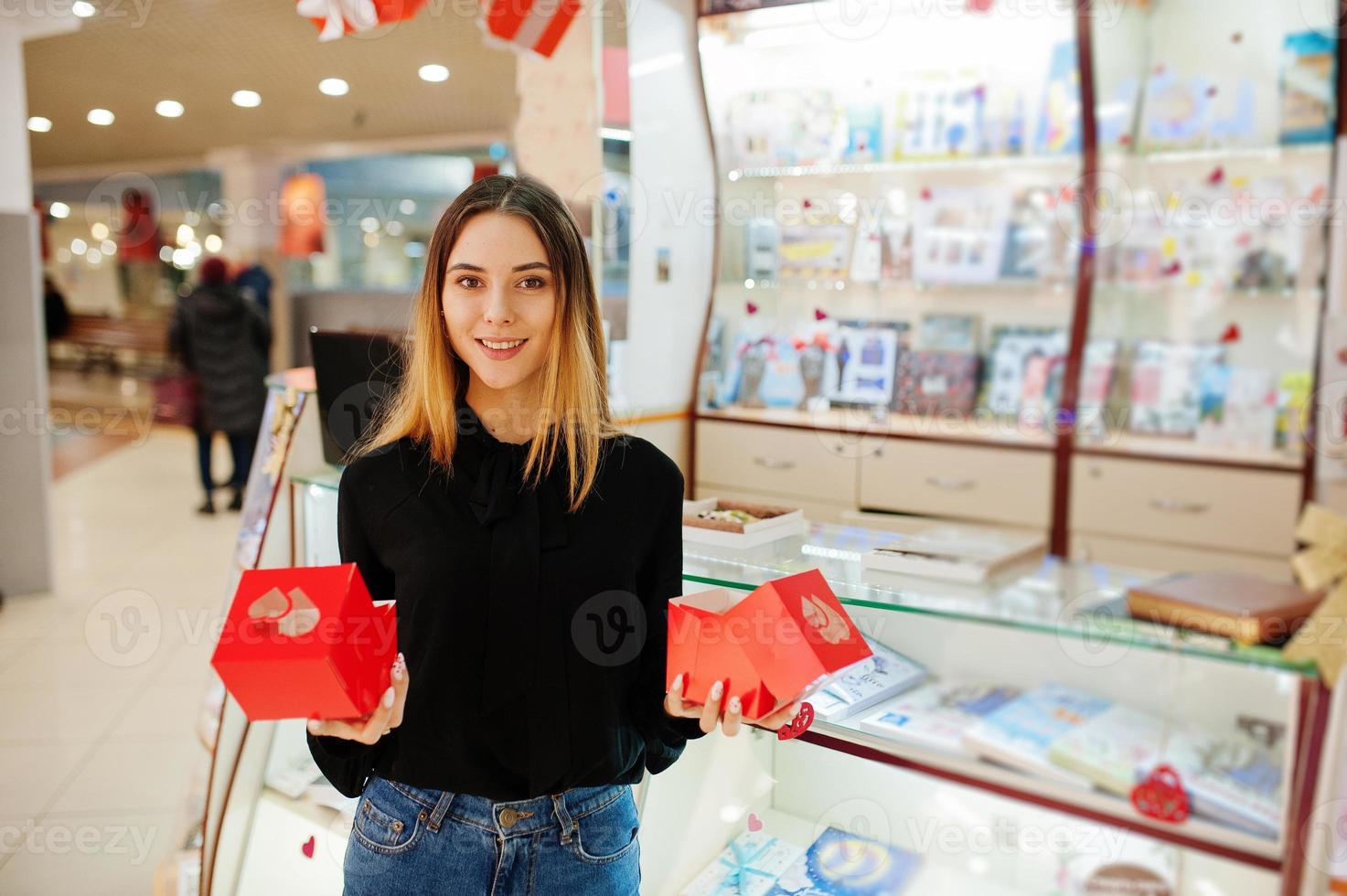 portret van jonge blanke vrouwelijke vrouw verkoper houdt rode geschenkdozen. klein bedrijf van snoep souvenirs winkel. foto