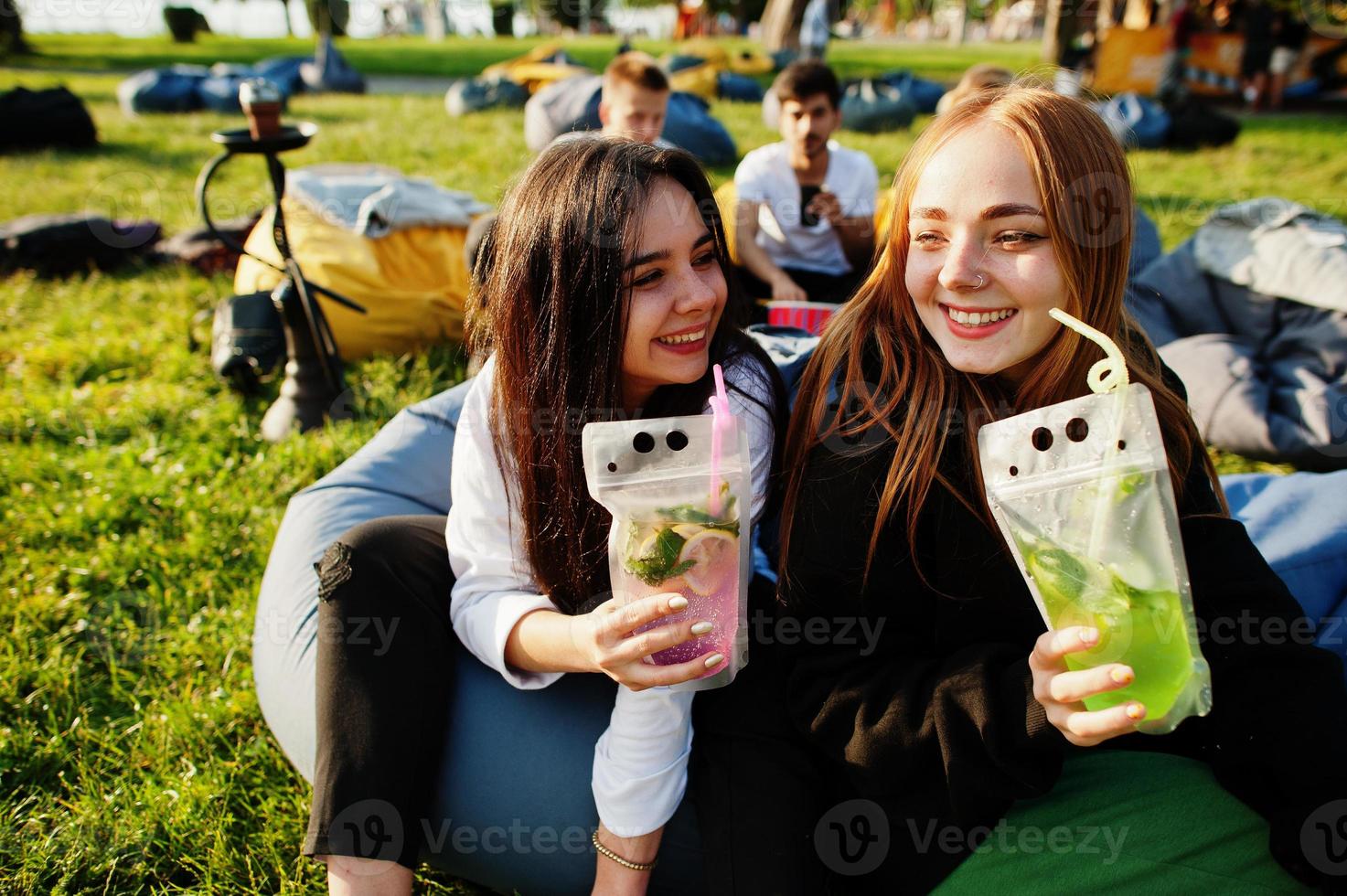 jonge multi-etnische groep mensen kijken naar film op poef in openluchtbioscoop. twee meisjes met mojitococktails. foto