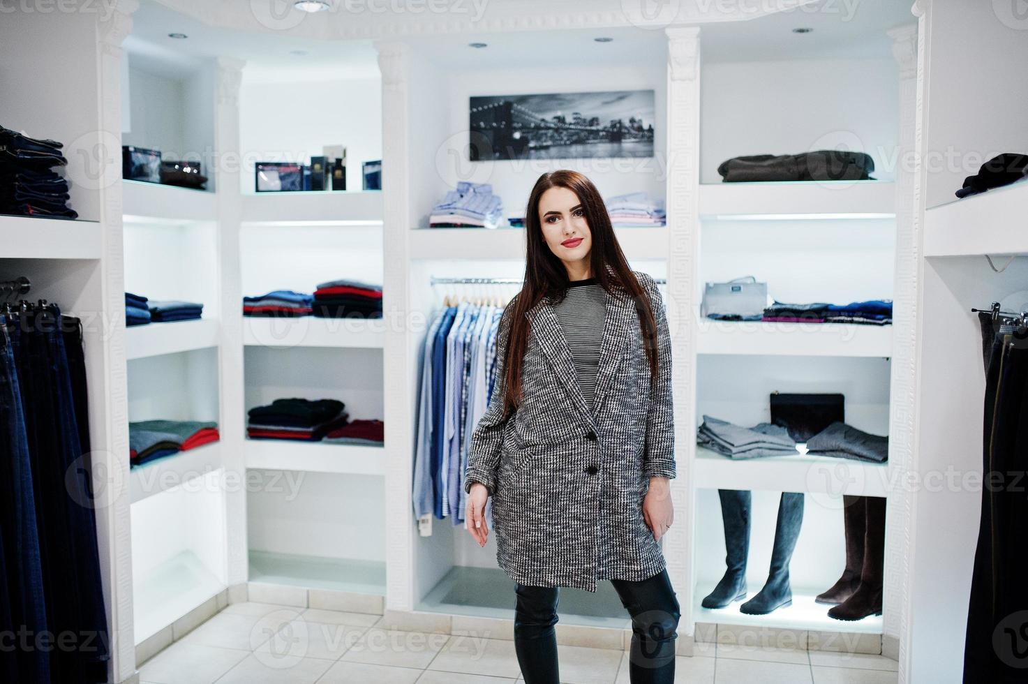 brunette prachtig meisje in de kledingwinkel boetiek bij casual kleding en grijze jas. foto