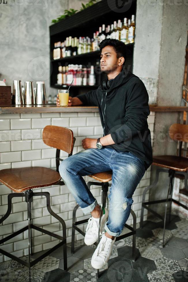 casual en stijlvolle jonge aziatische man met koptelefoon in café op bar sap drinken uit glas. foto