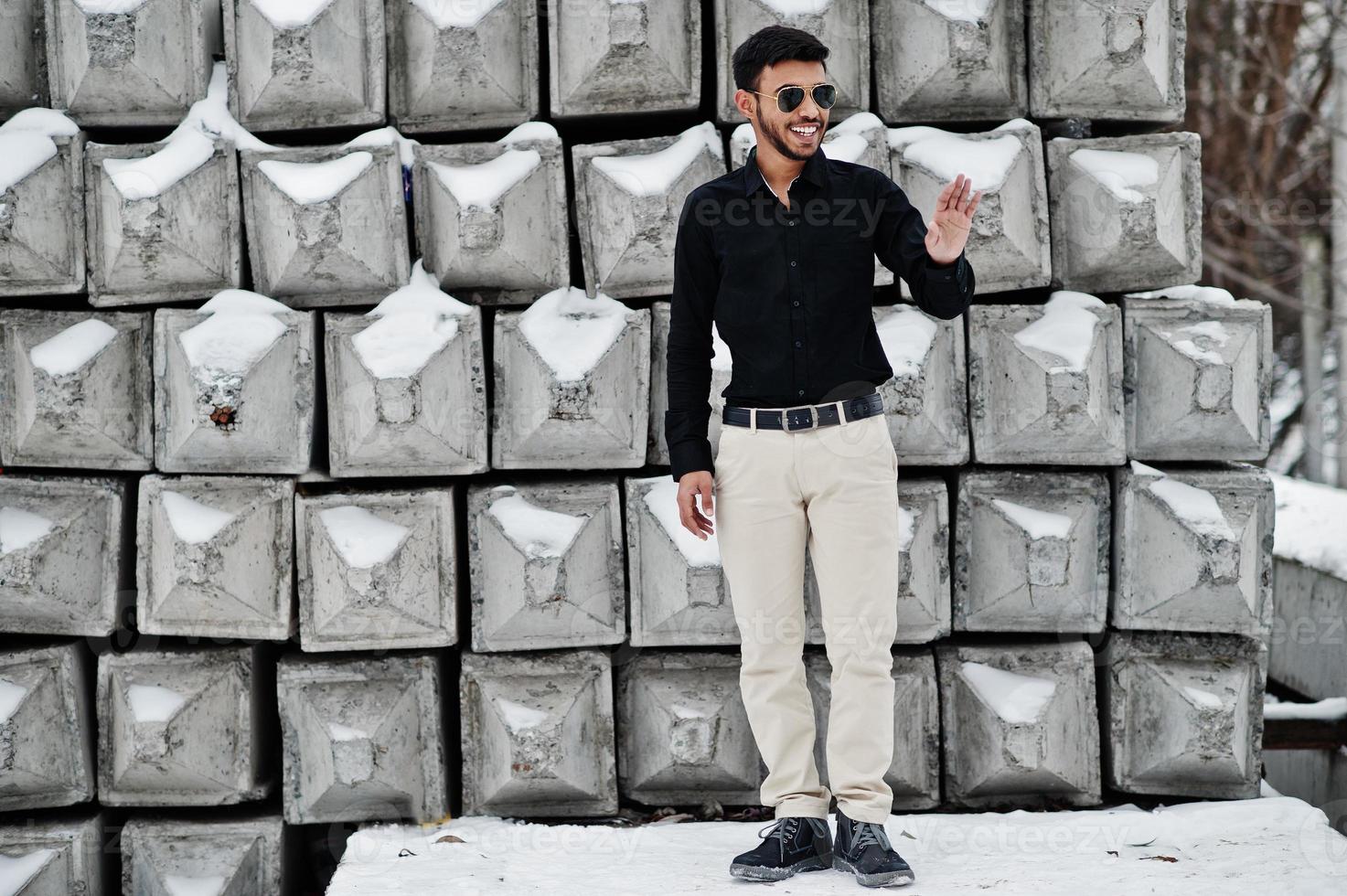 casual jonge Indiase man in zwart shirt en zonnebril poseerde tegen stenen blokken. foto