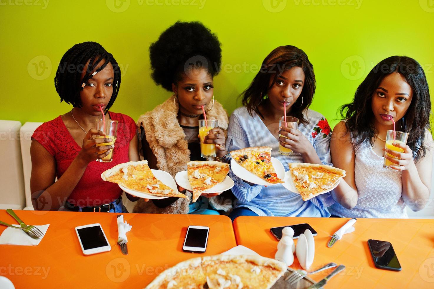 vier jonge afrikaanse meisjes in felgekleurd restaurant met pizzapunten op bord en sappen. foto