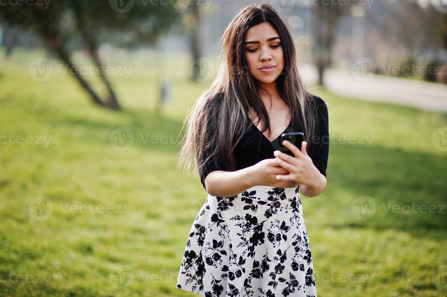 mooie latino model meisje uit ecuador dragen op zwarte tops en rok gesteld op straat met mobiele telefoon. foto