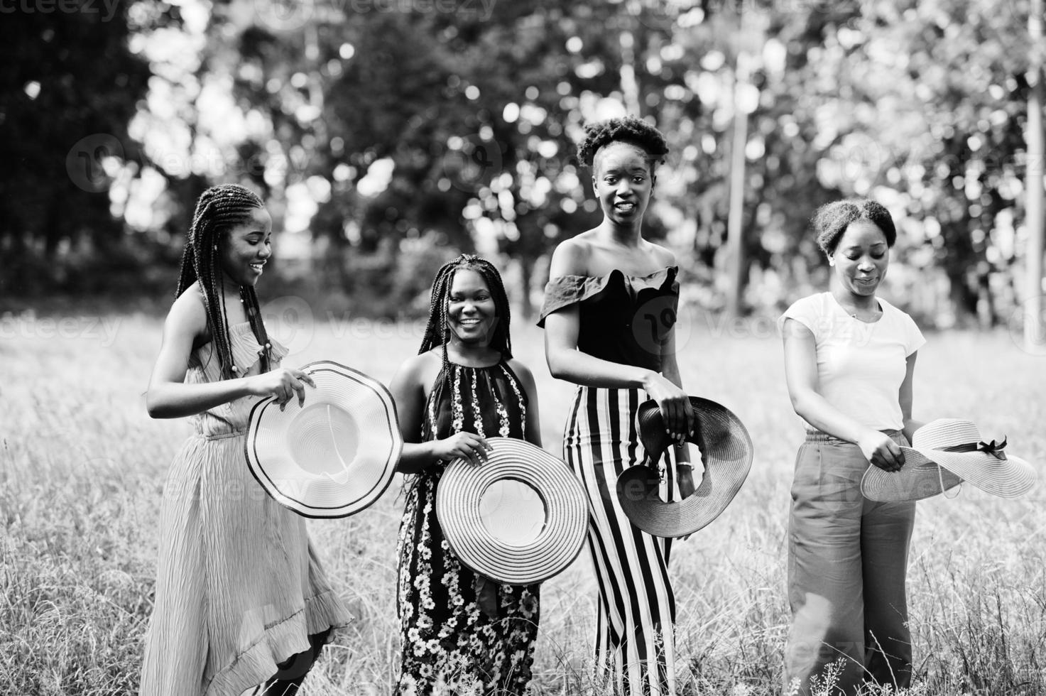 groep van vier prachtige Afro-Amerikaanse dames dragen een zomerhoed die tijd doorbrengt op groen gras in het park. foto