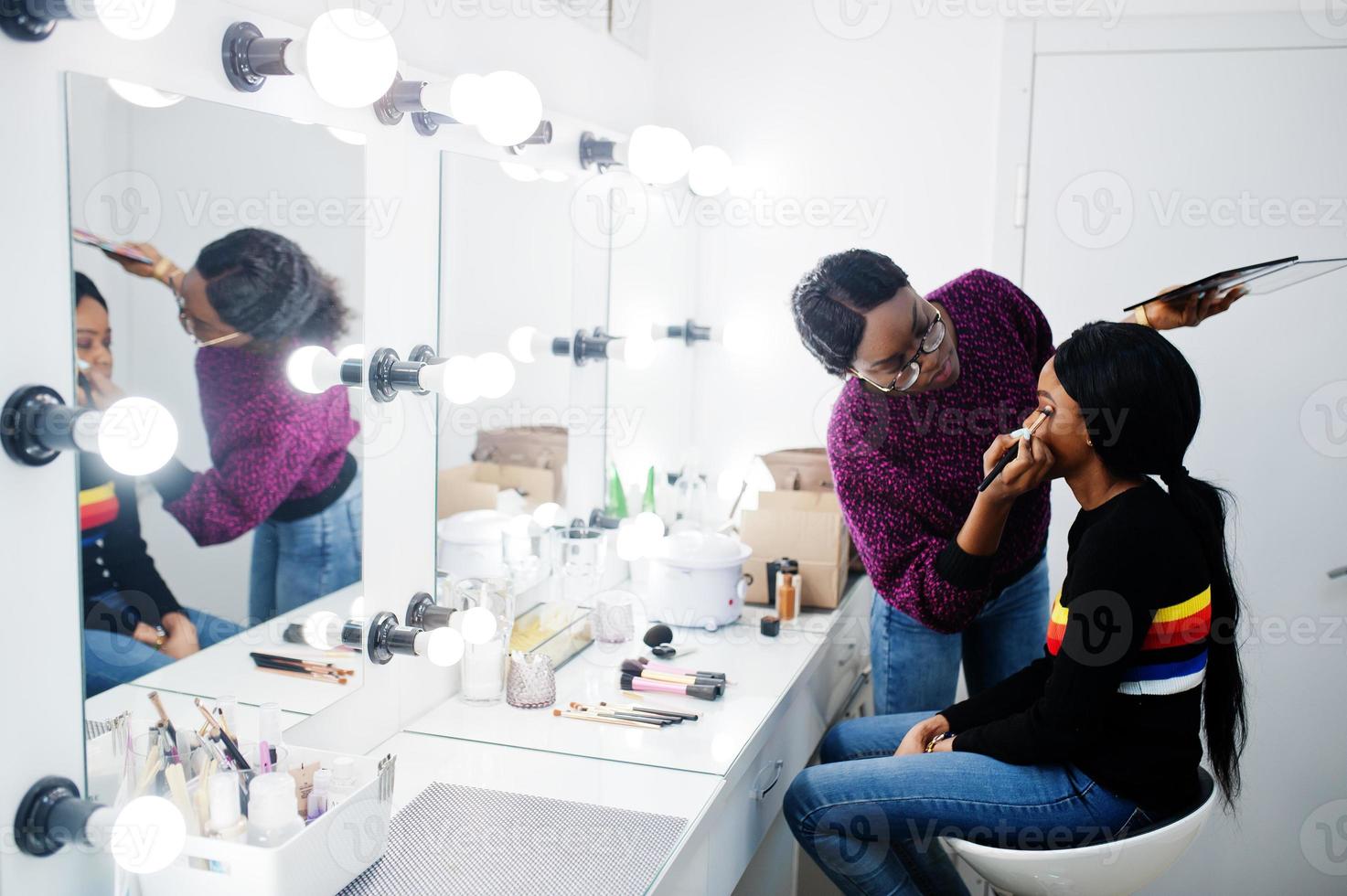 Afro-Amerikaanse vrouw die make-up toepast door visagist bij beauty salon. foto