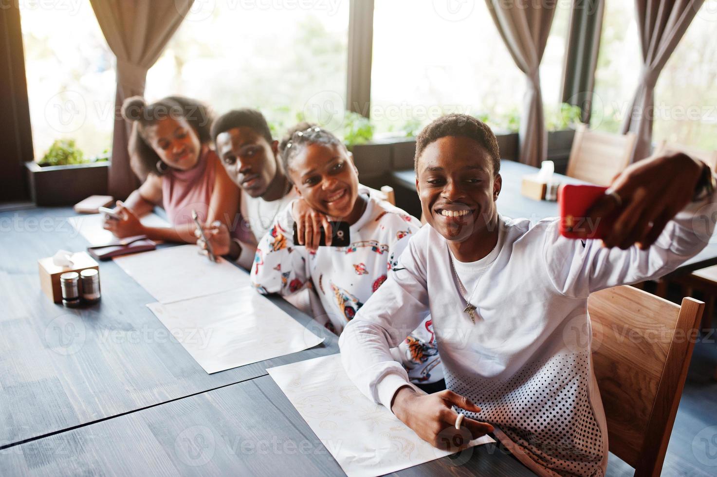 gelukkige Afrikaanse vrienden zitten en chatten in café. groep zwarte mensen die in restaurant samenkomen en naar hun mobiele telefoon kijken. foto