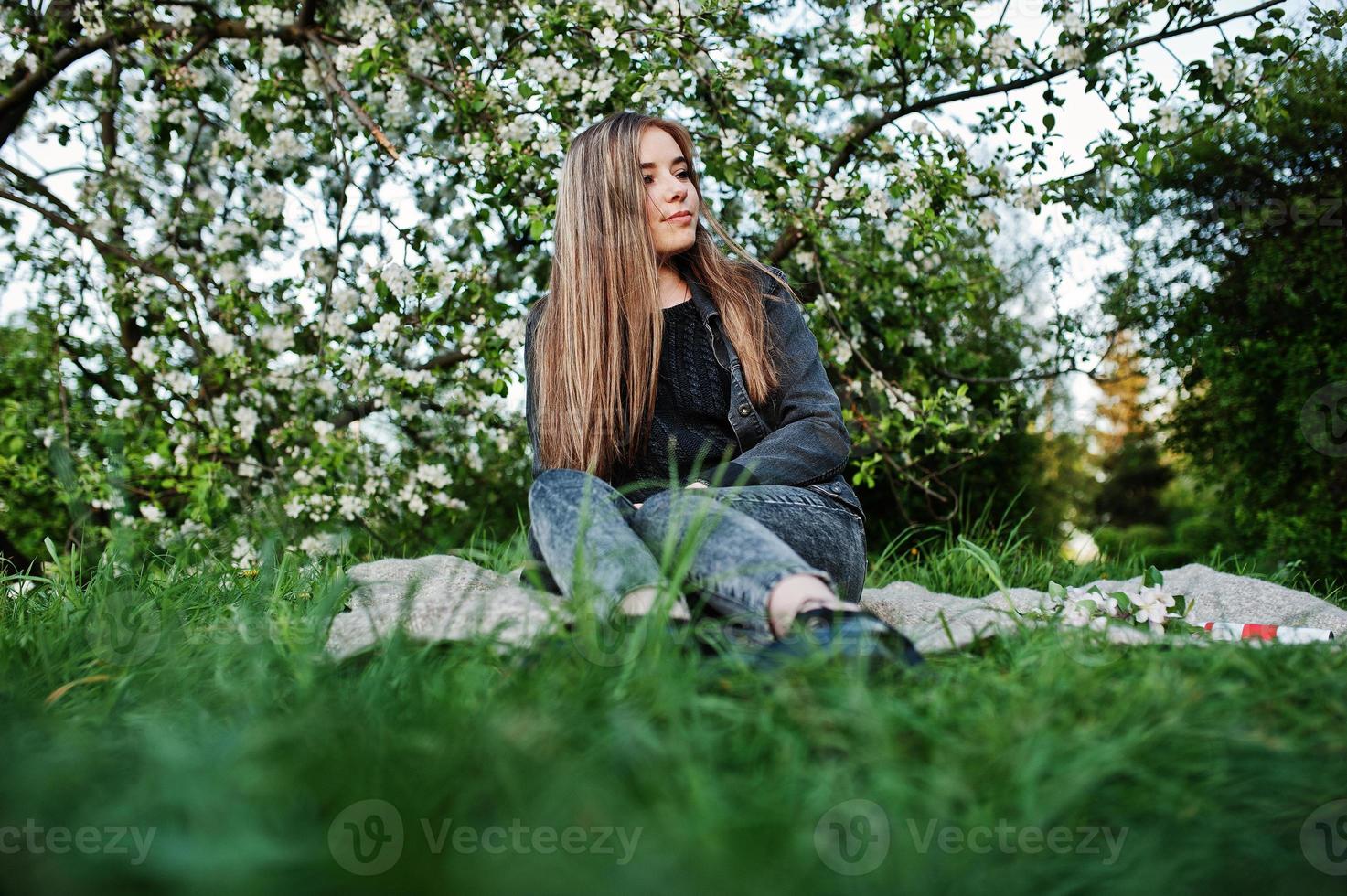 jonge brunette meisje op jeans zittend op plaid tegen lente bloesem boom. foto