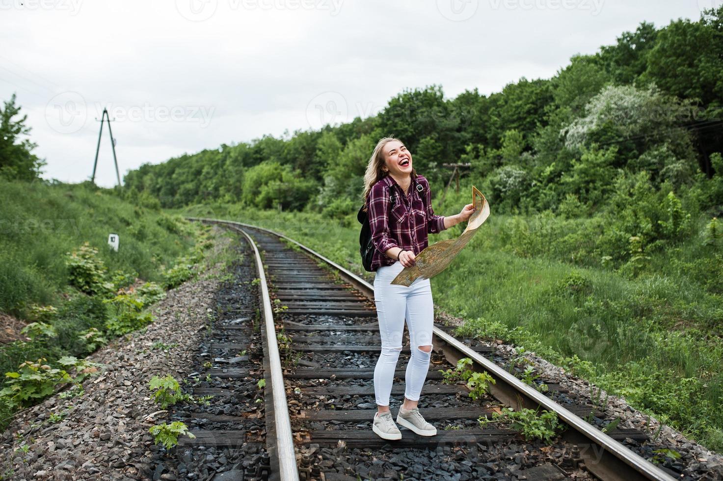 portret van een mooi blond meisje in tartan shirt wandelen op de spoorlijn met kaart in haar handen. foto