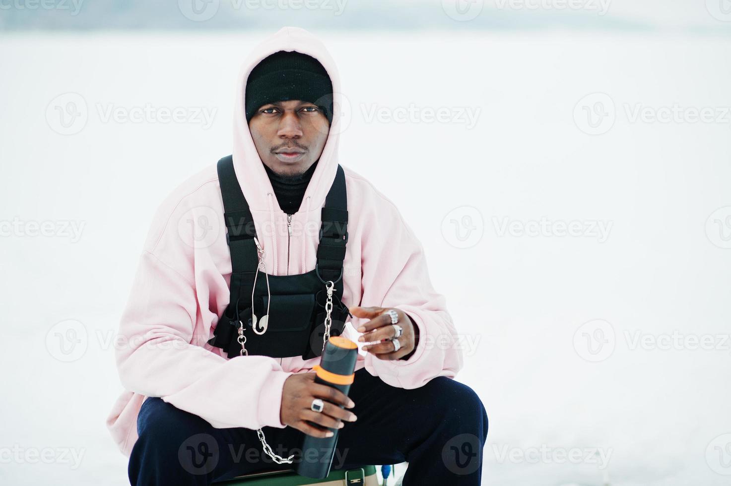 Afro-Amerikaanse visser met thermos zittend op bevroren meer. winter vissen. foto