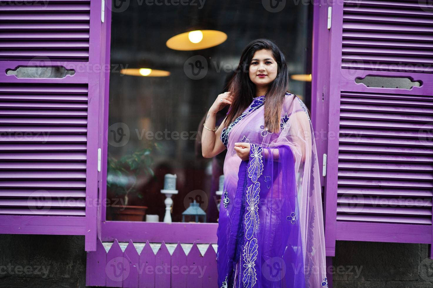 indiase hindoe meisje op traditionele violet saree poseerde op straat tegen paarse ramen. foto