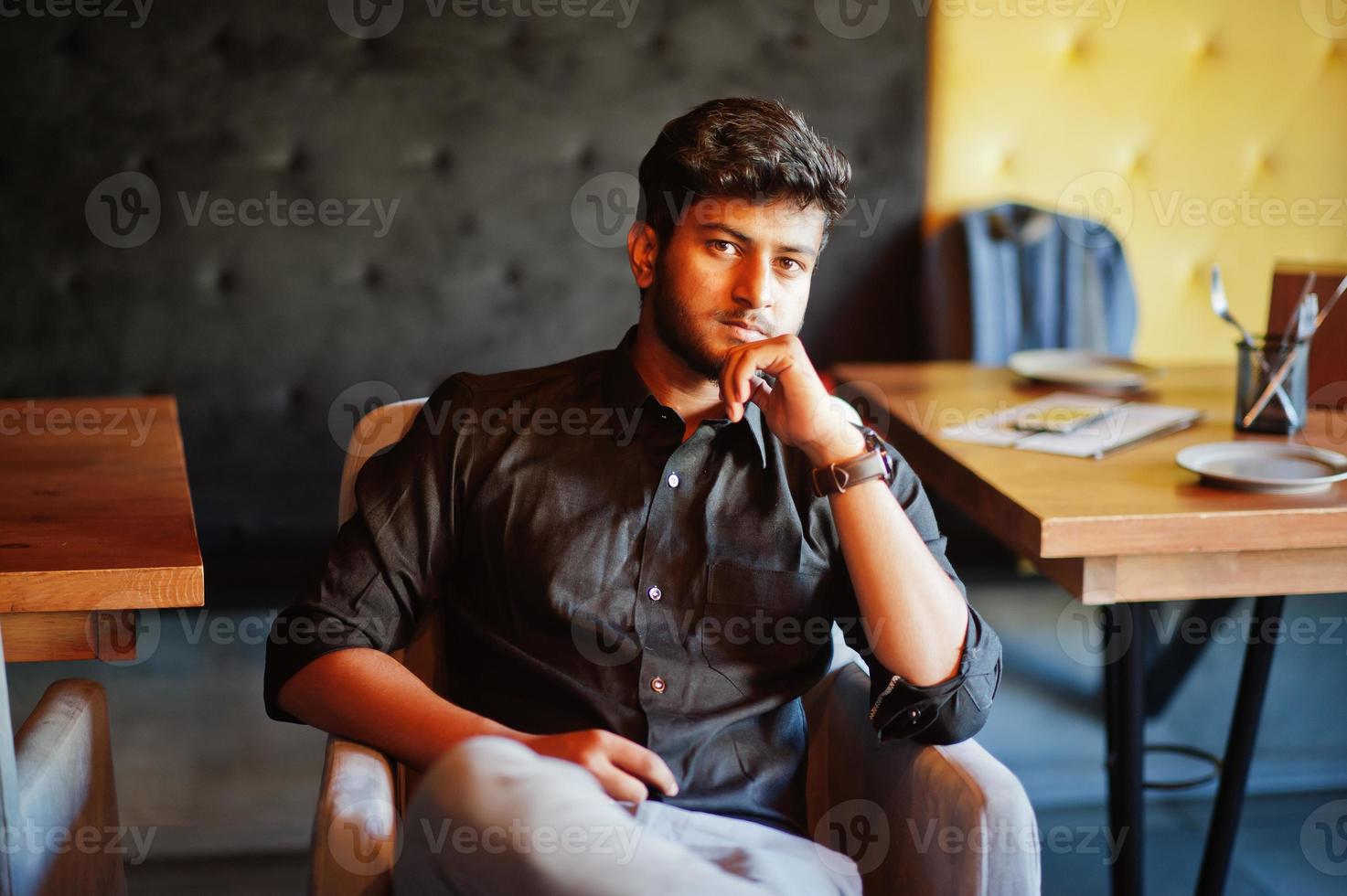zelfverzekerde jonge Indiase man in zwart shirt zit in café. foto