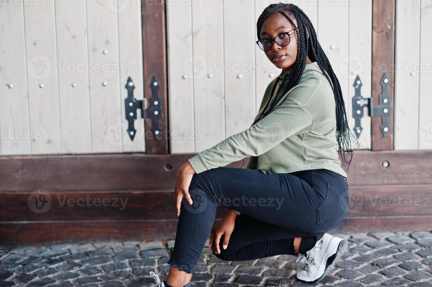 stadsportret van een positieve jonge vrouw met een donkere huid die een groene hoody en een bril draagt. foto