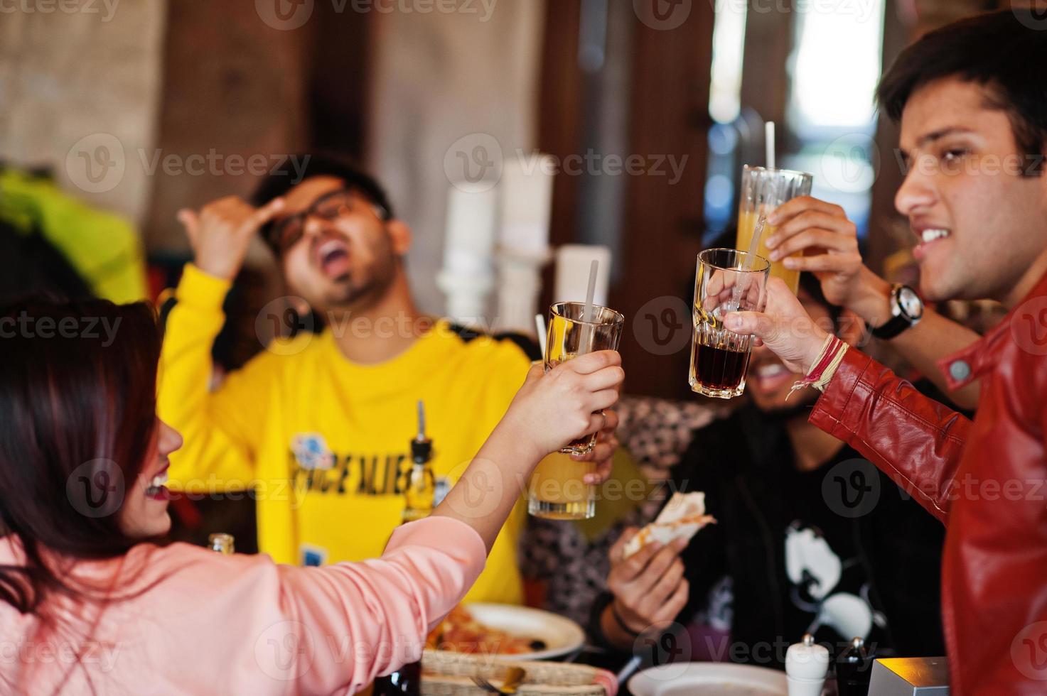 groep aziatische vrienden die pizza eten en juichen tijdens het feest bij pizzeria. gelukkige indiase mensen die samen plezier hebben, Italiaans eten en op de bank zitten. foto