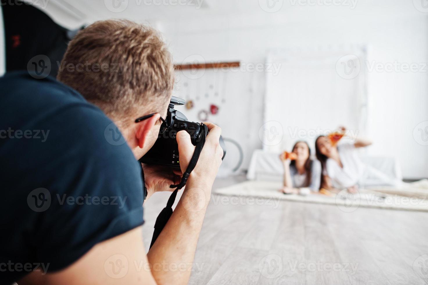 man fotograaf schieten op studio tweeling meisjes die pizza eten. professionele fotograaf op het werk. foto