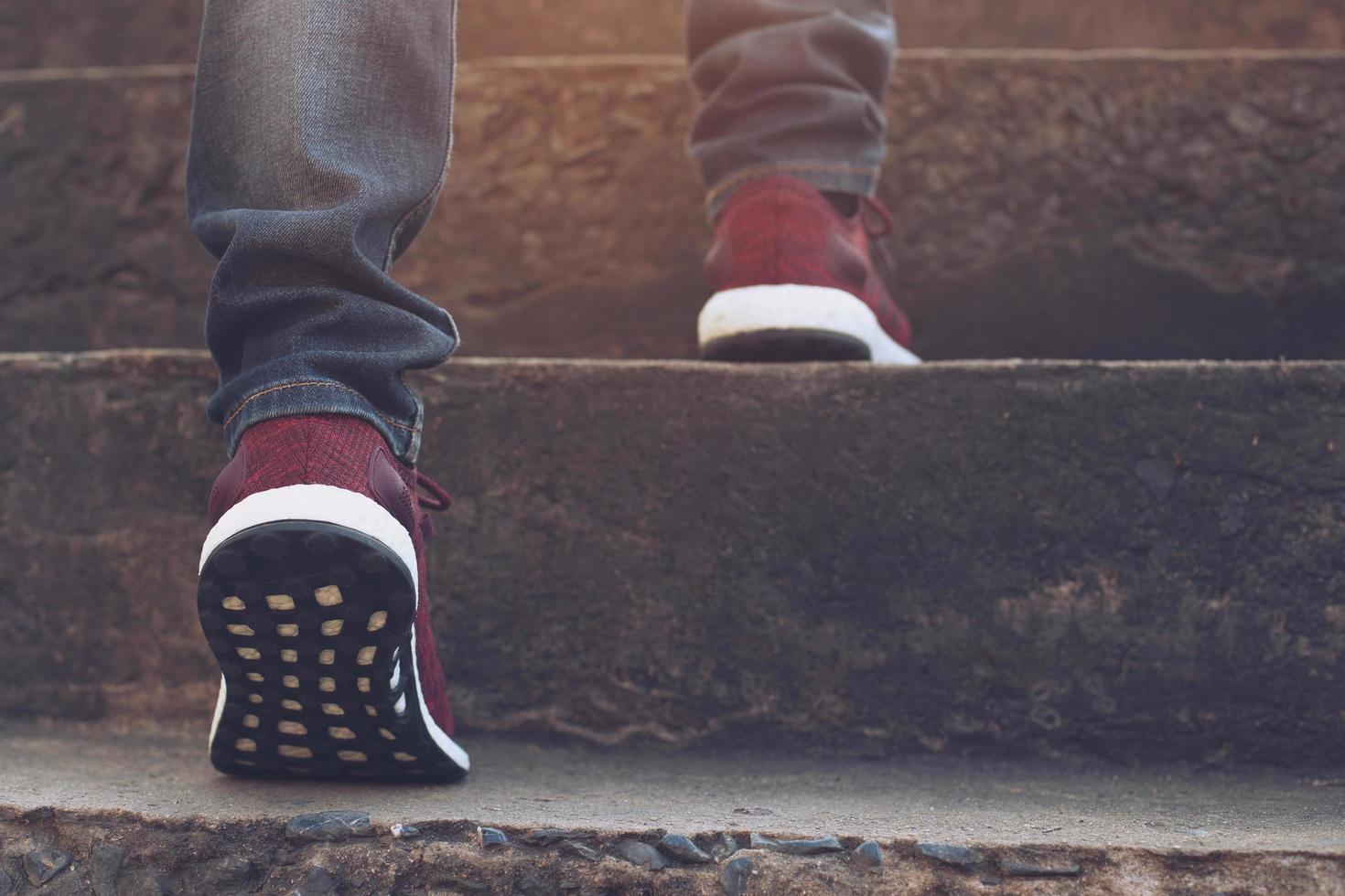 trap. close-up benen jeans en schoenen sneakers rood van jonge hipster man een persoon lopen intensivering de trap op gaan in de moderne stad, trap opgaan, succes, opgroeien. zonneschijn in de ochtend. foto