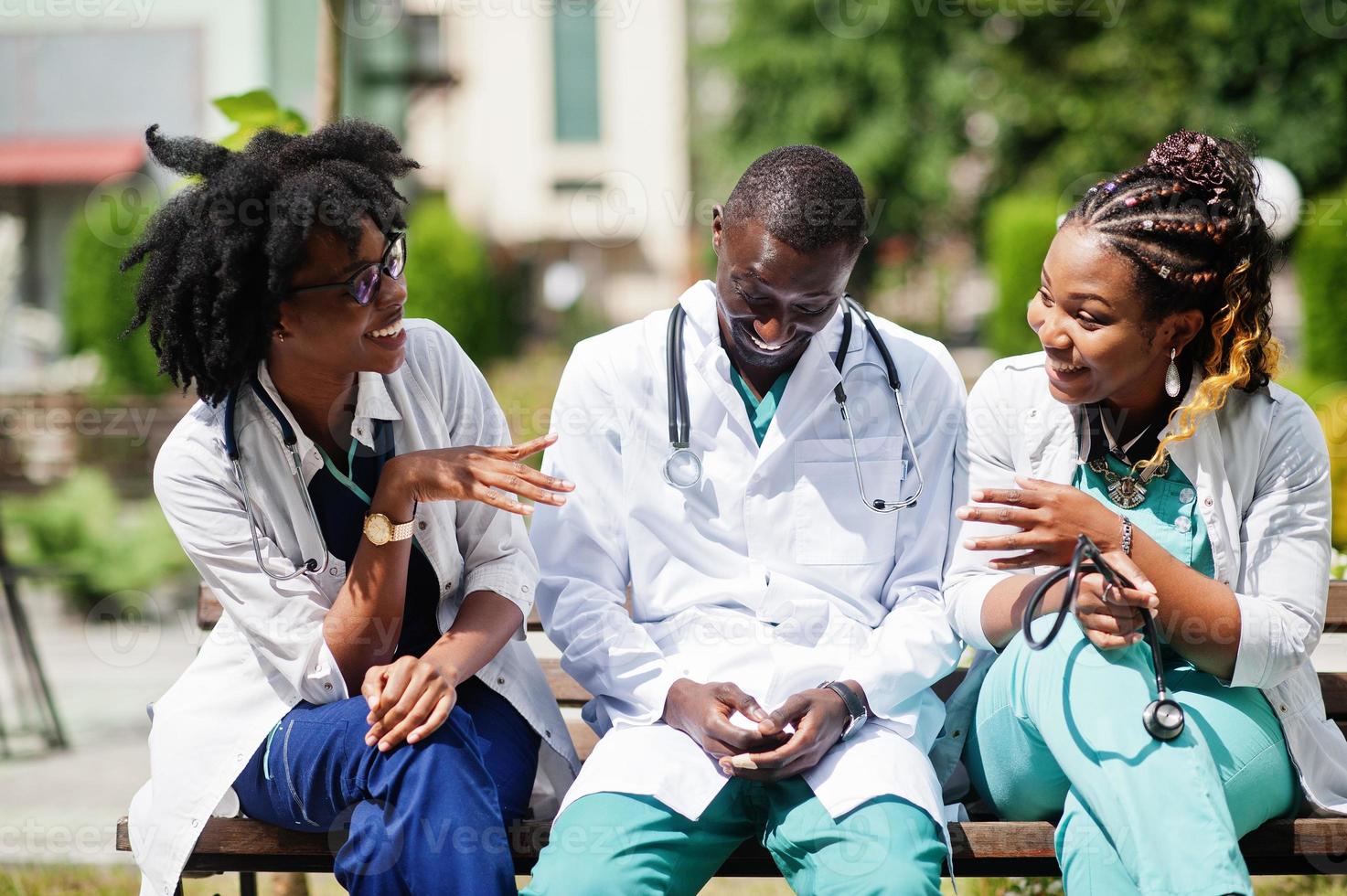 drie Afro-Amerikaanse groepsartsen met een stethoscoop die een laboratoriumjas draagt die op de bank zit. foto