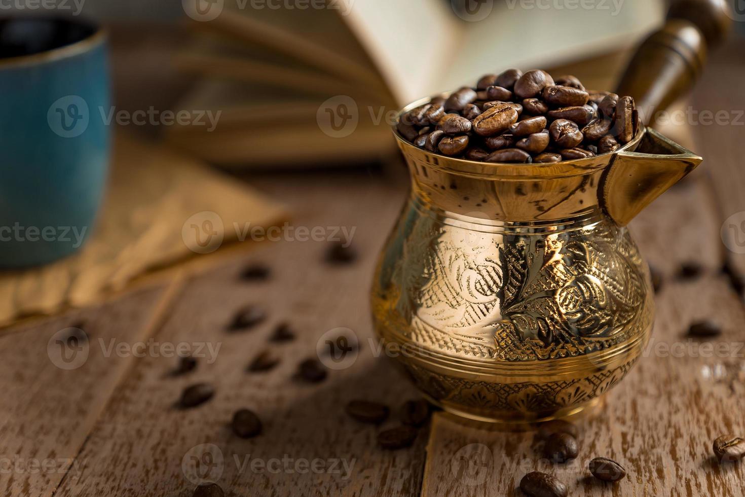 vers geroosterde koffiebonen in cezve traditionele Turkse koffiepot geopend boek en kopje op houten tafel. foto