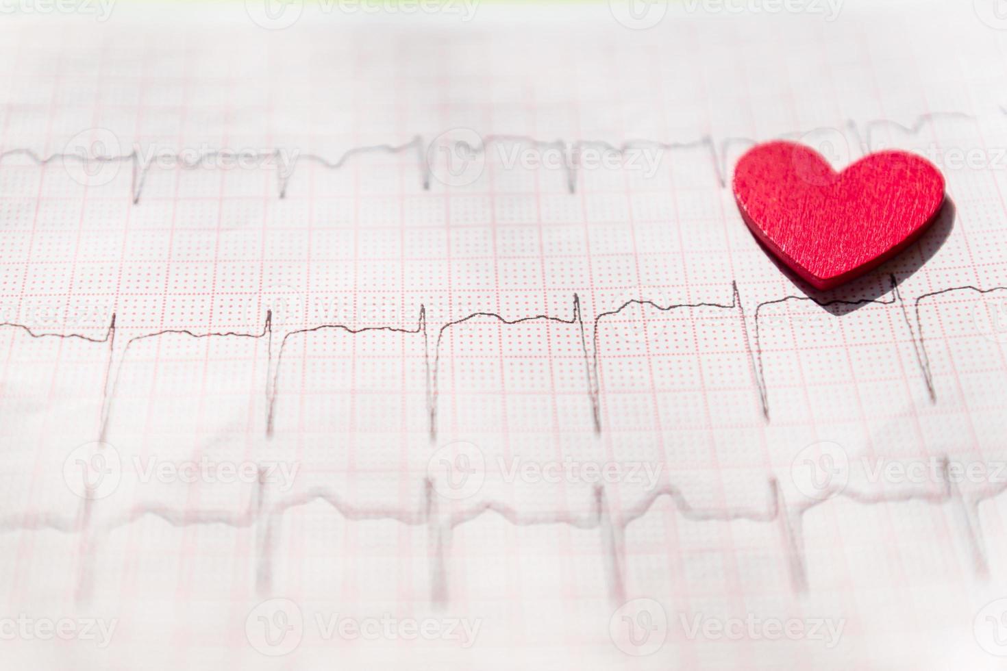 close-up van een elektrocardiogram in papieren vorm met rood houten hart. ecg of ekg papier achtergrond. medisch en gezondheidszorgconcept. foto