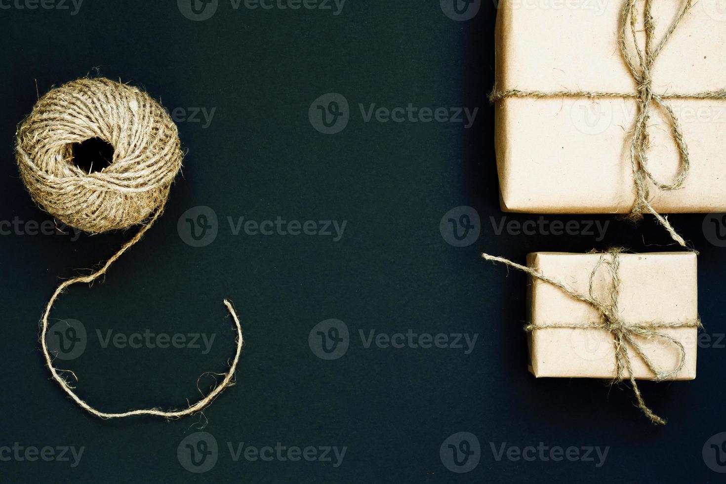 handgemaakte geschenkdoos verpakt in ambachtelijk papier met rood houten hart, touw en strik op zwarte achtergrond. bovenaanzicht, plat gelegd foto