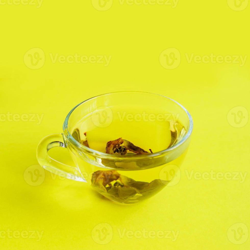 transparante beker met groene thee op gele achtergrond. foto
