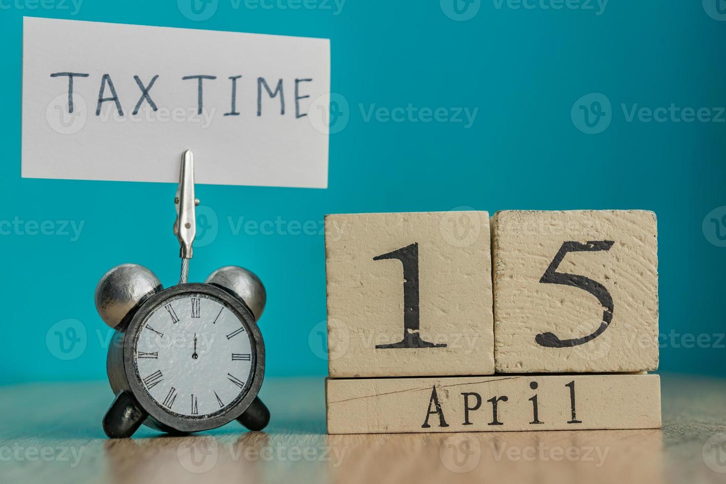 belastingdag herinnering concept. 15 april houten kalender en wekker met banner en handgeschreven zin belastingtijd op houten tafel. foto