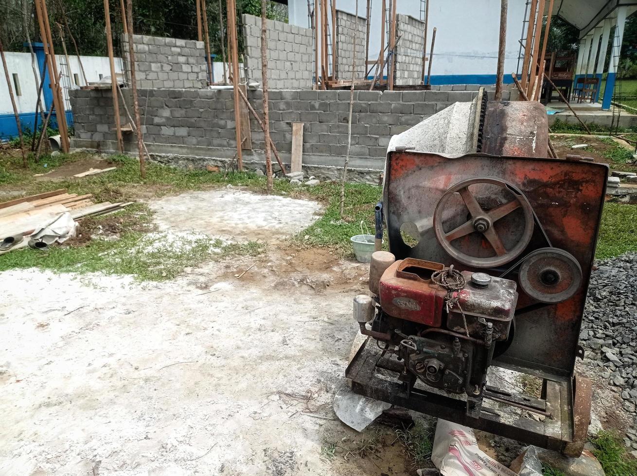 een betonmixer geïnstalleerd op een bouwplaats naast een hoop zand en grind. foto